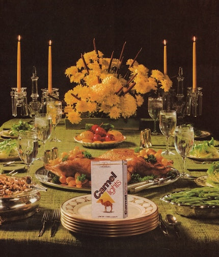 Dinner table set with food and Camel Light cigarettes on a dark background