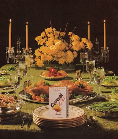 Dinner table set with food and Camel Light cigarettes on a dark background