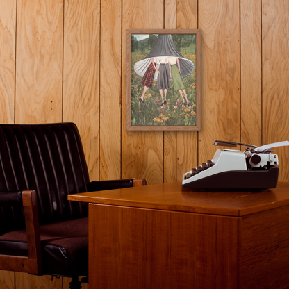 A framed art print depicting three women standing in a field, displayed on a wood-paneled wall above a wooden desk with a vintage typewriter and a dark leather office chair.