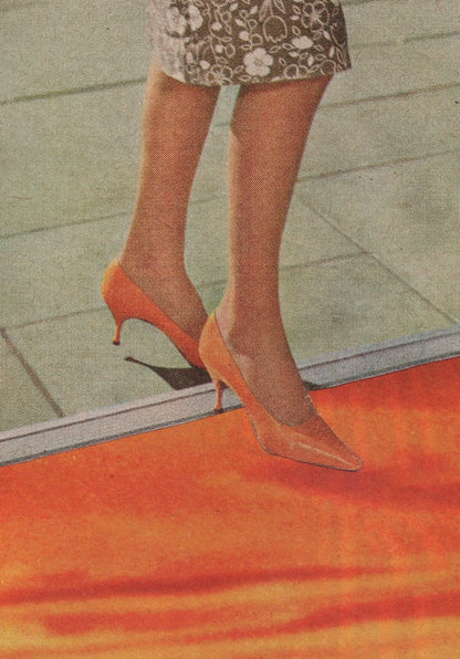 A close-up of a person's legs wearing pointed-toe high heels in a warm orange or peach tone, standing on a red-orange surface with a tiled floor in the background.