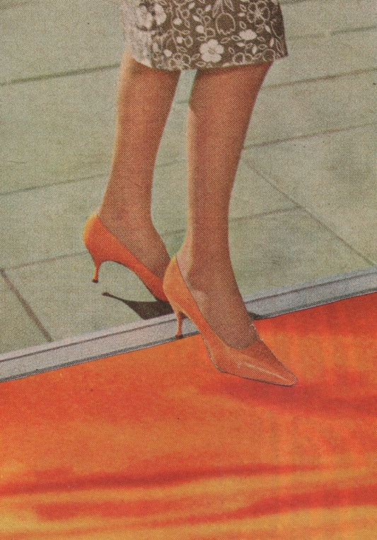 A close-up of a person's legs wearing pointed-toe high heels in a warm orange or peach tone, standing on a red-orange surface with a tiled floor in the background.